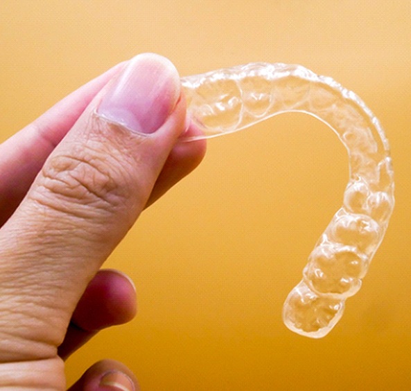 An up-close look at a customized Invisalign aligner being held by a thumb and forefinger