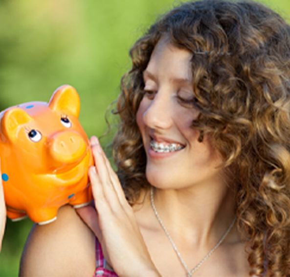 Woman with braces in Frisco smiling at an orange piggy bank