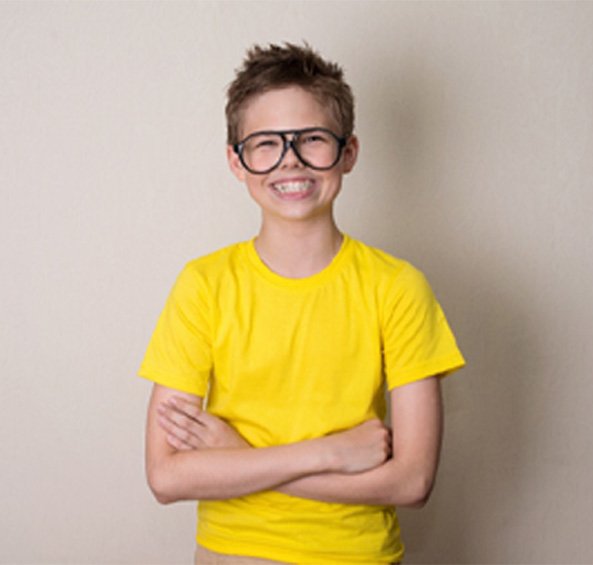 Boy with glasses and yellow shirt smiling proudly showing off his braces in Frisco