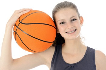 Smiling girl with braces in Frisco holding a basketball on her shoulder 