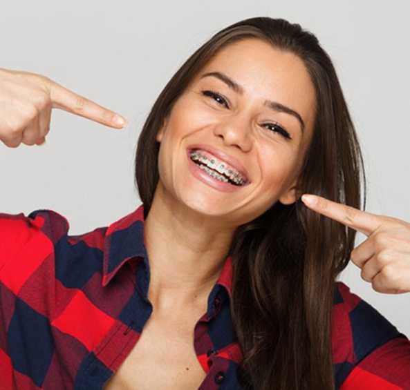 Smiling young woman in a flannel shirt pointing to her braces