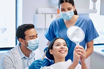 Dentist and dental assistant smiling while patient looks at teeth in mirror
