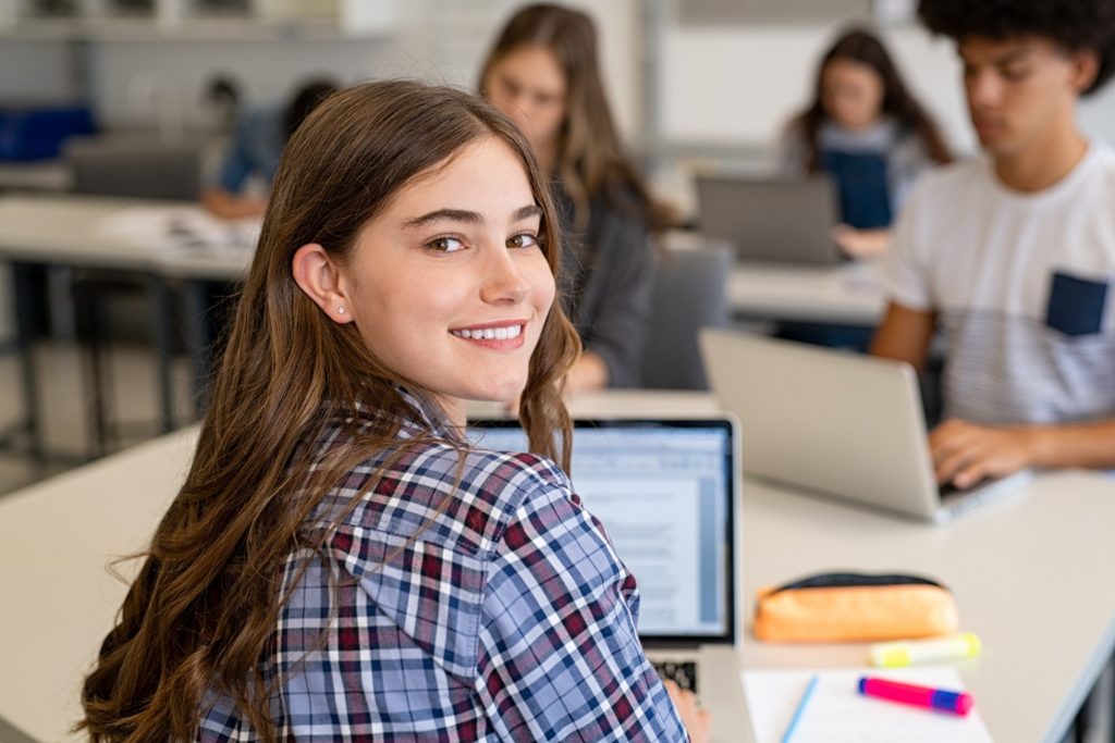Teen girl smiling while working on computer in classroom